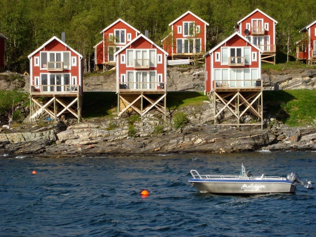 Røde rorbuer på påler sett fra fjorden, med en båt foran