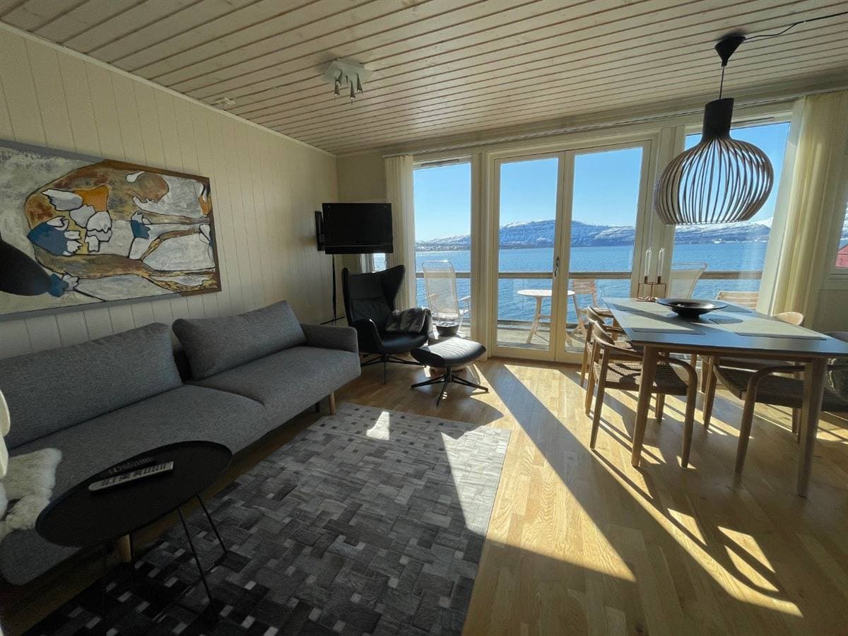 Stue og spisekrok i leiligheten med fjordutsikt gjennom balkongdørene